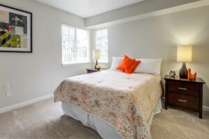 Bedroom with queen size mattress, 2 nightstands, neutral toned carpeting and wall paint, well lit window