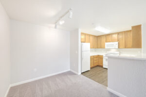 Unit Dining area and kitchen, light brown cabinetry and wood like floors in kitchen, white appliances, ceiling lights.