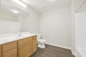 Unit Bathroom, wood like floors, bathtub/shower, light brown cabinetry, large vanity mirror, white countertop.