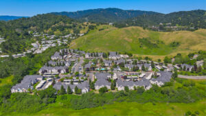 Aerial Exterior of Bay Vista at Meadow Park, Sprawling Hills in the distance, trees scattered throughout the property, photo taken on a sunny day.