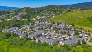 Aerial Exterior of Bay Vista at Meadow Park, Sprawling Hills in the distance, trees scattered throughout the property, photo taken on a sunny day.